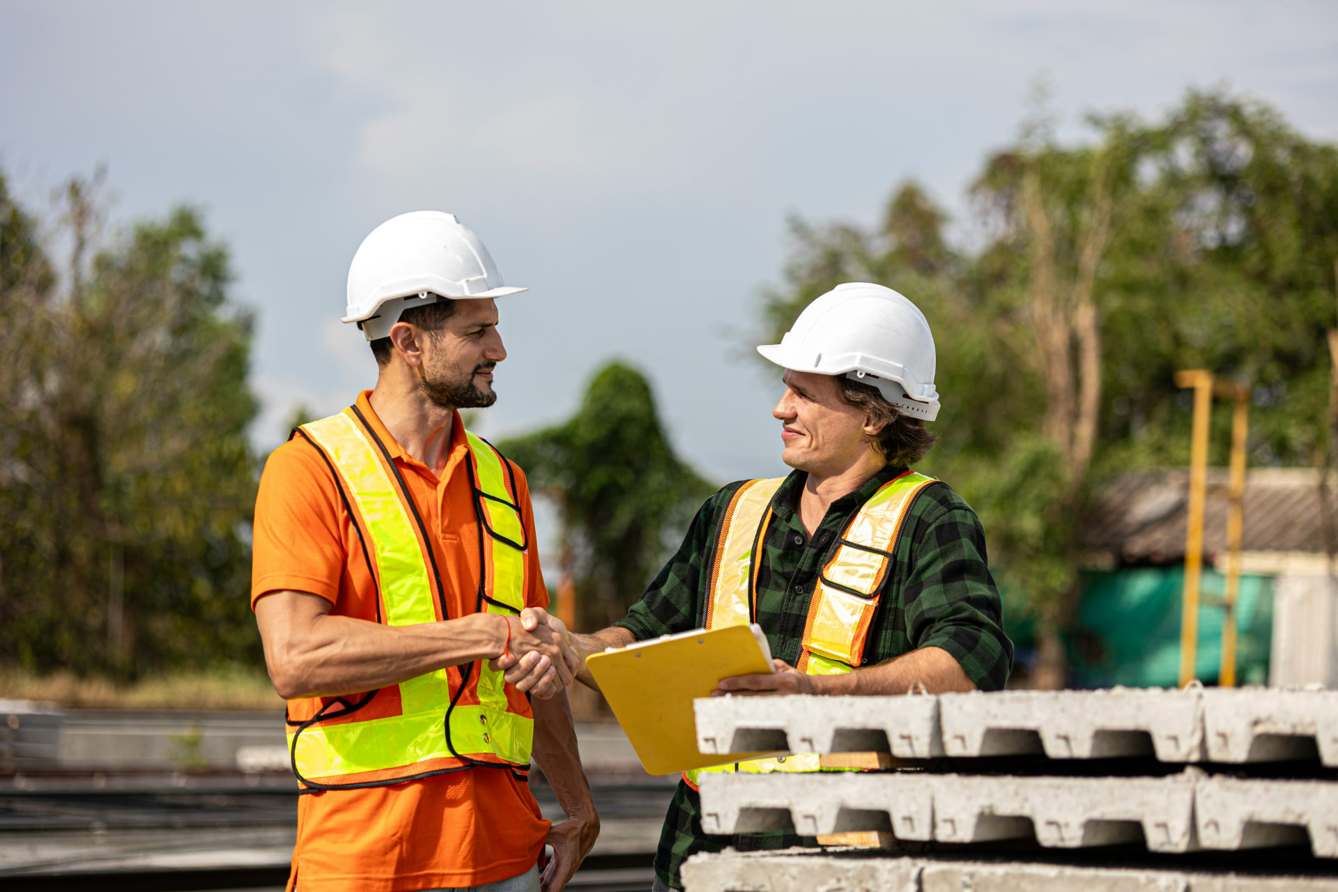 Two contractors in safety vests and hard hats shaking hands at a Wichita job site
